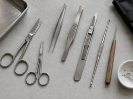 Ciseaux, pinces, scalpel, sonde, aiguille et épingles disposés sur une paillasse.
